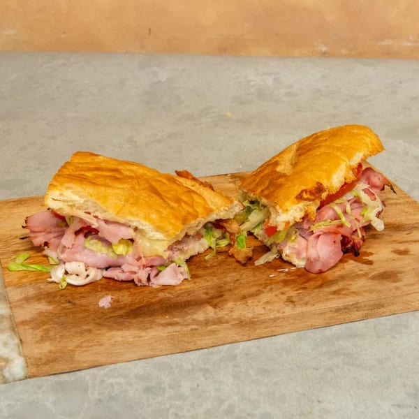 A large deli sandwich, cut in half, filled with meat, lettuce, and tomatoes on a wooden board.