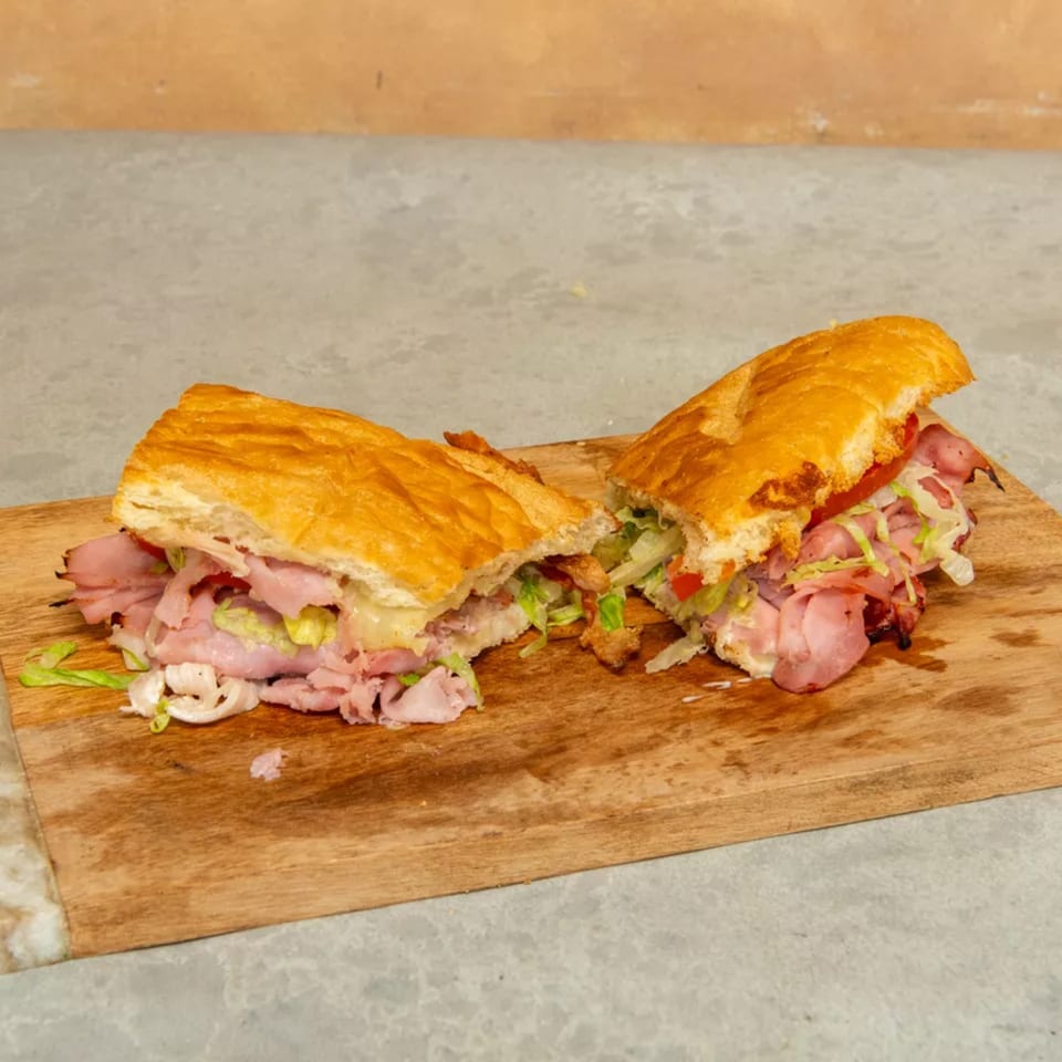A large deli sandwich, cut in half, filled with meat, lettuce, and tomatoes on a wooden board.