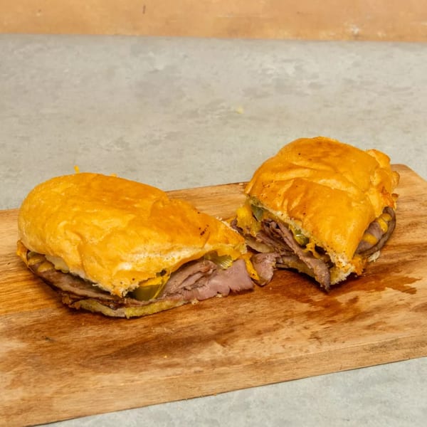 A Cuban sandwich, cut in half, revealing roasted pork, ham, Swiss cheese, pickles, and mustard.