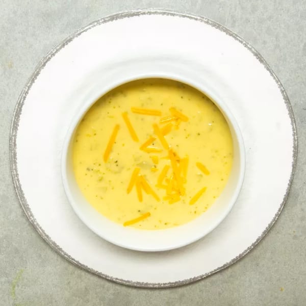 Creamy broccoli cheddar soup in a white bowl, garnished with shredded cheese.