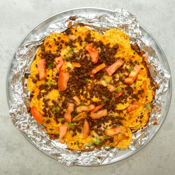 A round pan of nachos with melted cheese, ground beef, diced tomatoes, and green onions.