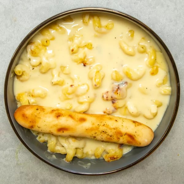 Creamy macaroni and cheese with a golden-brown breadstick on a dark plate.