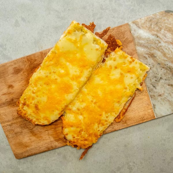 Two golden-brown cheese toasts on a wooden board, with a marble and concrete background.