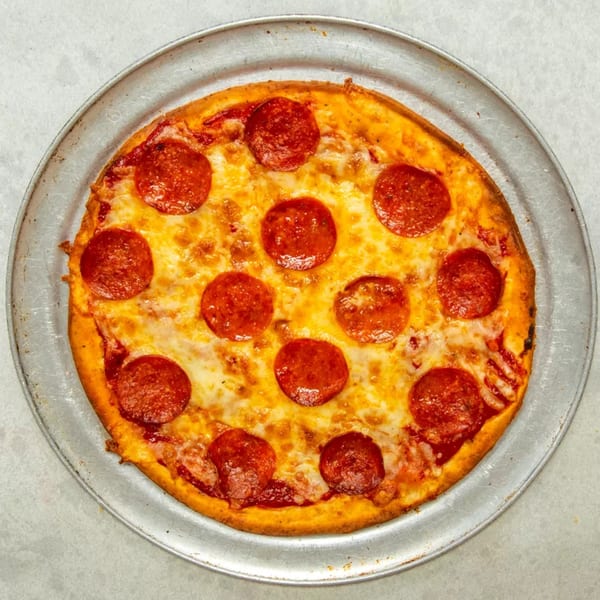 A round pepperoni pizza with melted cheese and a golden crust sits on a metal pan.
