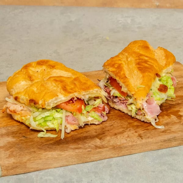 Two halves of a large sandwich with meat, lettuce, and tomato on a wooden board.
