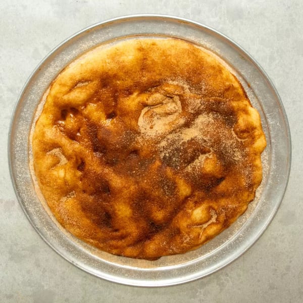 A golden-brown dessert pizza, sprinkled with cinnamon sugar, rests on a metal pan.